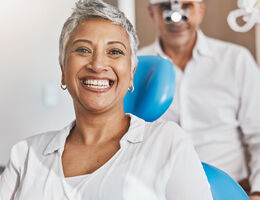 A smiling woman in a dentist chair with a dentist behind her.