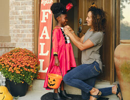 A girl with a Halloween bucket smiles as a woman adjusts her costume.