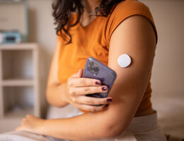 A woman holds a phone near her continuous glucose monitor.