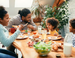 A family shares a meal as the dad leans forward to laugh with his two sons.