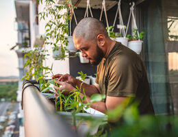 A man tends plants on an apartment balcony.